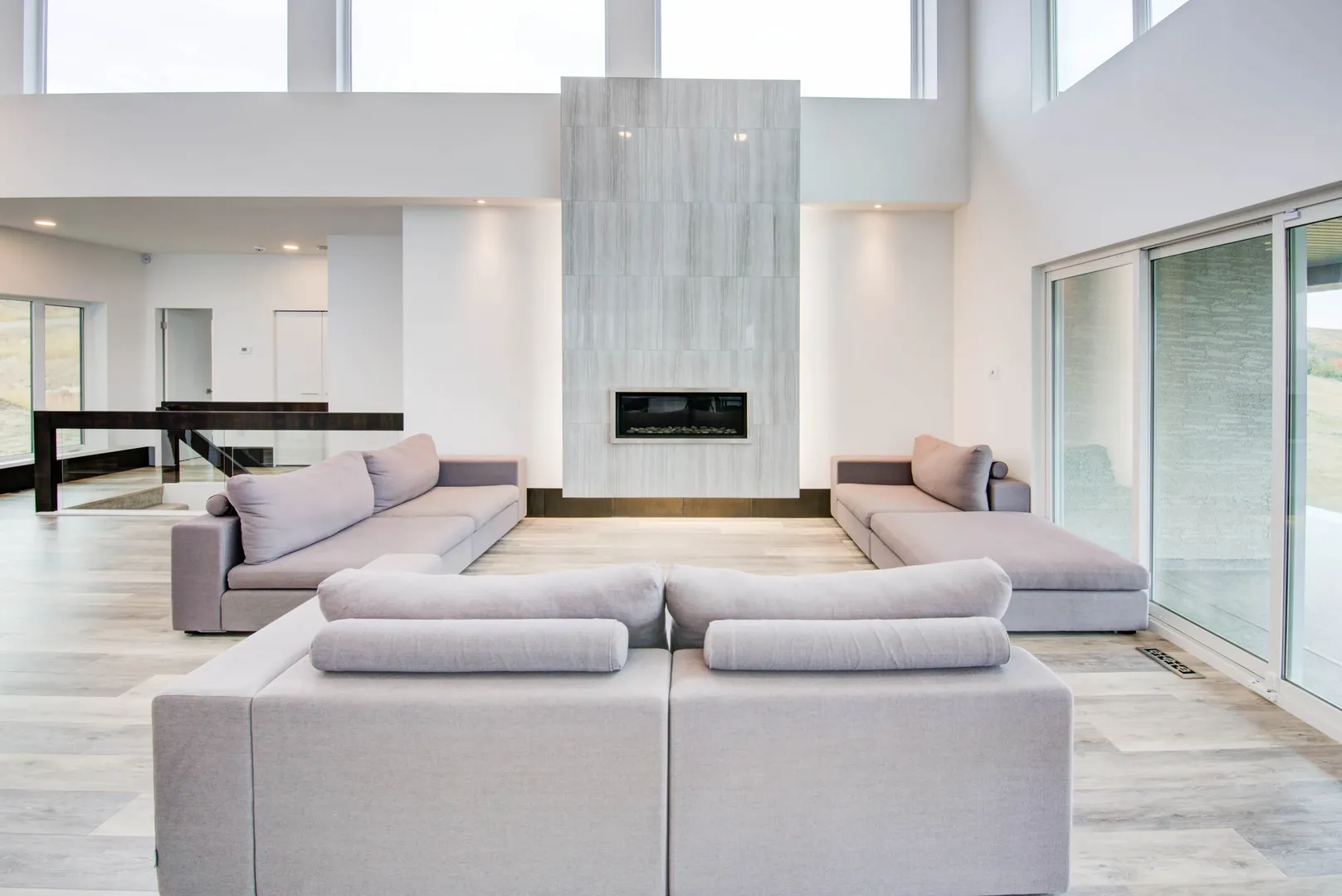 Double-height living room with pale sofas, a tall stone fireplace and expansive windows